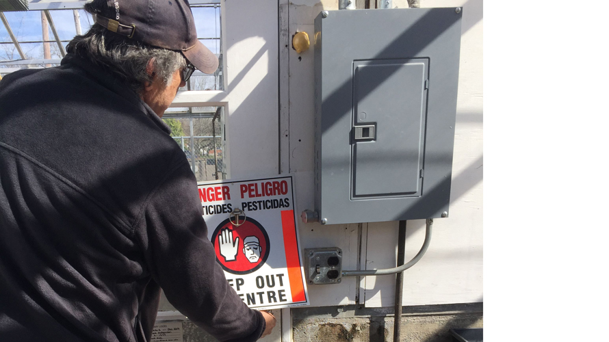 Greenhouse worker making adjustments to sign reading, "Danger, Keep Out"