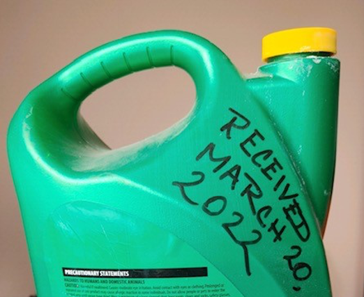 Contenedor de pesticidas con fecha recibida escrito por mano.