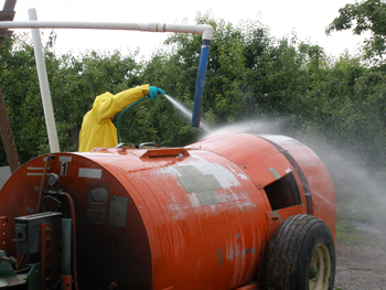 Worker in yellow protective suit sprays off an orange pesticide container.